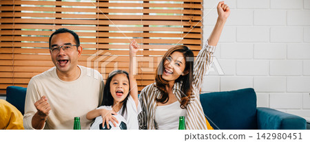 A happy family enjoys the thrill of a football match at home A happy family enjoys the thrill of a football match at home 142980451
