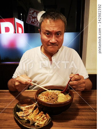 一位胃口很好的中年男子喜歡吃札幌味噌拉麵和煎餃。 一位胃口很好的中年男子喜歡吃札幌味噌拉麵和煎餃。 142981592