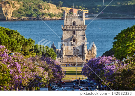 Jacaranda trees bloom by Belem Tower at sunset on the Tagus River Jacaranda trees bloom by Belem Tower at sunset on the Tagus River 142982323