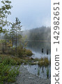 The quiet lake reflects the peaceful beauty of the autumn landscape. 142982651