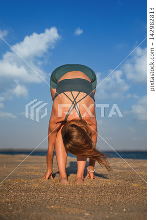 Woman practicing Uttanasana on sandy beach at sunset Woman practicing Uttanasana on sandy beach at sunset 142982813
