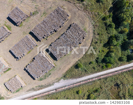 Aerial view of piled dark blocks at heat power station site. Rectangular stacks fill gravel yard near tree line, suggesting fuel or material storage in stark industrial setting with calm order. Aerial view of piled dark blocks at heat power station site. Rectangular stacks fill gravel yard near tree line, suggesting fuel or material storage in stark industrial setting with calm order. 142983108
