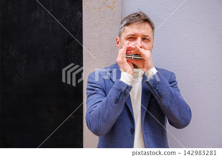 Man plays harmonica outdoors in city street Man plays harmonica outdoors in city street 142983281