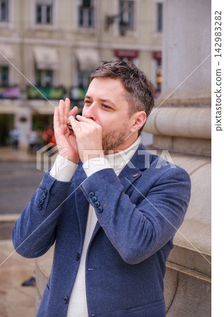 Man plays harmonica outdoors in city street Man plays harmonica outdoors in city street 142983282