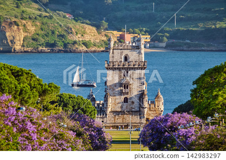 Scenic Belem Tower in Lisbon framed by blooming jacaranda trees during sunset Scenic Belem Tower in Lisbon framed by blooming jacaranda trees during sunset 142983297