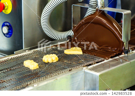 Process of glazing marzipan candies with chocolate on chocolate tempering machine at factory 142983528