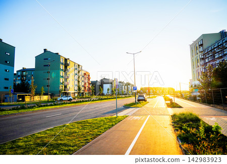 Sunrise lighting up city street with condominium complex buildings and parked cars Sunrise lighting up city street with condominium complex buildings and parked cars 142983923