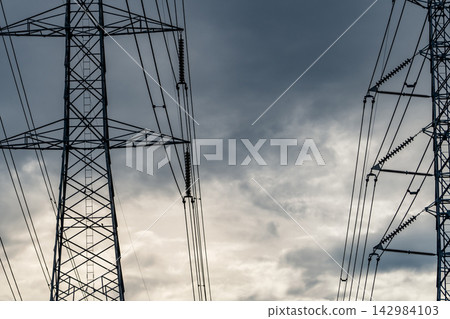 High voltage electricity pylons with transmission cables and insulators against stormy clouds, electrical grid infrastructure for reliable power transmission and energy distribution network. High voltage electricity pylons with transmission cables and insulators against stormy clouds, electrical grid infrastructure for reliable power transmission and energy distribution network. 142984103