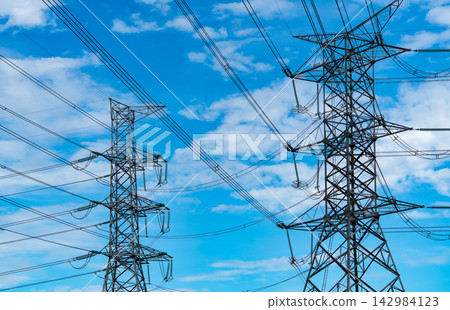 High voltage electricity transmission towers and power lines against blue cloudy sky, large scale electrical grid infrastructure supplying energy for cities, industry and modern development. High voltage electricity transmission towers and power lines against blue cloudy sky, large scale electrical grid infrastructure supplying energy for cities, industry and modern development. 142984123
