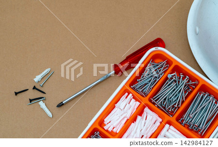 Hardware organizer filled with screws and plastic anchors beside screwdriver on work surface, useful equipment for wall mounting, furniture assembly, renovation and home improvement projects Hardware organizer filled with screws and plastic anchors beside screwdriver on work surface, useful equipment for wall mounting, furniture assembly, renovation and home improvement projects 142984127