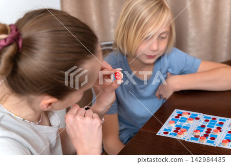 Two people enjoying a game together, one holding a token with a number while the other observes, creating a moment of educational bonding and entertainment at home Two people enjoying a game together, one holding a token with a number while the other observes, creating a moment of educational bonding and entertainment at home 142984485
