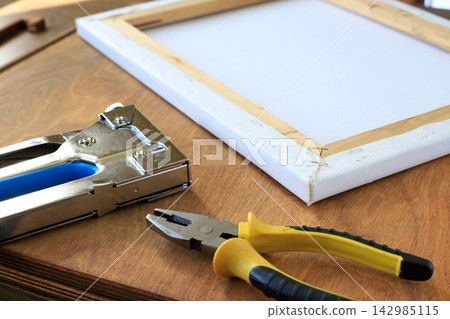 Canvas Stretching Tools with Stapler and Pliers Beside Stretcher Frame on Table. Art Studio Concept Canvas Stretching Tools with Stapler and Pliers Beside Stretcher Frame on Table. Art Studio Concept 142985115