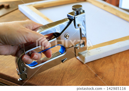 Hand Stapling Canvas Edge to Wooden Stretcher Frame with Metal Tacker. Art Mounting Concept Hand Stapling Canvas Edge to Wooden Stretcher Frame with Metal Tacker. Art Mounting Concept 142985116