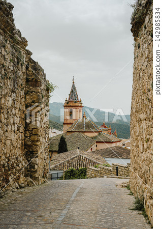 Stone alley framing a domed church bell tower with a tiled spire Stone alley framing a domed church bell tower with a tiled spire 142985834
