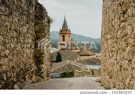 Stone alley framing a domed church bell tower with a tiled spire Stone alley framing a domed church bell tower with a tiled spire 142985835