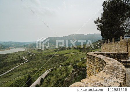 Stone castle wall overlooking a green valley, reservoir, and winding road Stone castle wall overlooking a green valley, reservoir, and winding road 142985836