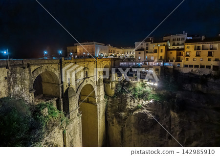 Puente Nuevo bridge glows above the illuminated cliffside restaurants of Ronda at night Puente Nuevo bridge glows above the illuminated cliffside restaurants of Ronda at night 142985910
