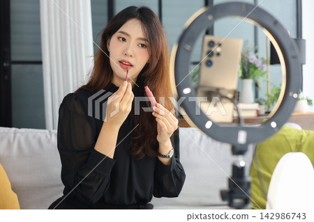 Young Asian influencer filming a beauty makeup tutorial video at home. 142986743