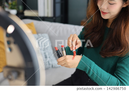 Young woman holding lipstick tubes options, beauty blogger reviewing makeup cosmetics products close up. Young woman holding lipstick tubes options, beauty blogger reviewing makeup cosmetics products close up. 142986750