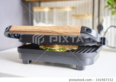 Sandwich maker grilling sandwich with bread, cheese and lettuce on kitchen counter Sandwich maker grilling sandwich with bread, cheese and lettuce on kitchen counter 142987152