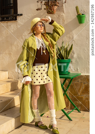 Trendy fashionista in lime raincoat and polka dot skirt on sunny urban day 142987196