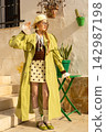 Fashionable young woman in lime green trench coat and polka dot skirt against white urban wall 142987198