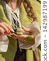Woman holding matcha mug with artistic nails and green attire in sunlight 142987199