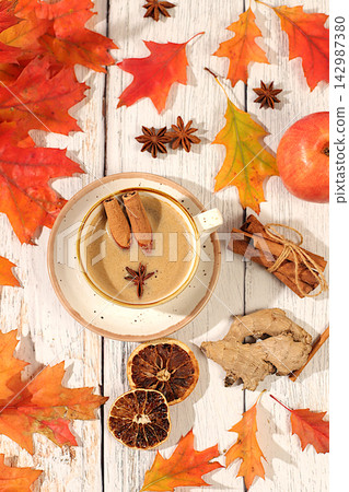 Indian masala chai with milk, ginger, anise, and cinnamon on an old wooden table with fallen autumn leaves. A traditional seasonal drink with spices, a cafe advertising card, a restaurant menu. 142987380