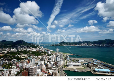 從海峽夢塔眺望關門大橋和關門海峽,以及夏日天空下的下關市和門司市的城市景觀。 從海峽夢塔眺望關門大橋和關門海峽,以及夏日天空下的下關市和門司市的城市景觀。 142987576