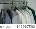 In the closet, checkered, dark and gray jackets hang on a chrome crossbar, close to a row of snow-white and light blouses on hangers. Concept: standard organization of clothes, contrast of textures 142987592