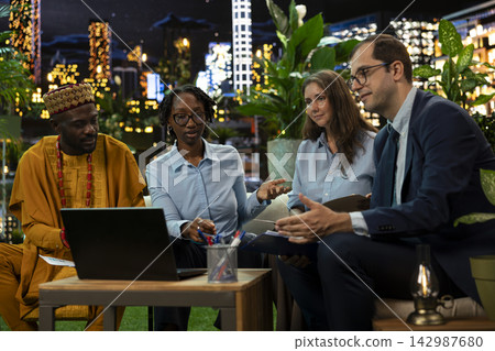 Coworkers looking at laptop display during remote international call, participating in brainstorming session from rooftop terrace at night. Business team discussing data during teleconference meeting Coworkers looking at laptop display during remote international call, participating in brainstorming session from rooftop terrace at night. Business team discussing data during teleconference meeting 142987680