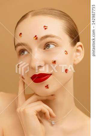 Beautiful girl with glitter on her face on peach isolated background. Happy woman in love with red lipstick. Valentine's day concept. International women's day. Vertical photo. Advertisement Beautiful girl with glitter on her face on peach isolated background. Happy woman in love with red lipstick. Valentine's day concept. International women's day. Vertical photo. Advertisement 142987755