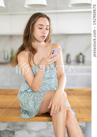 Young woman scrolling smartphone in kitchen Young woman scrolling smartphone in kitchen 142988678
