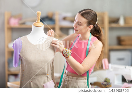 Woman seamstress adjusts clothes on mannequin Woman seamstress adjusts clothes on mannequin 142988703