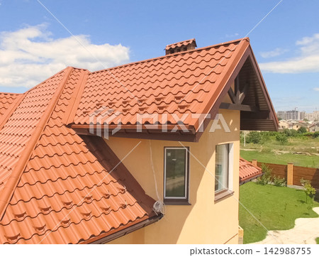House with a new roof made of orange metal. View from above. Corrugated metal roof and metal roofing. Modern roof made of met House with a new roof made of orange metal. View from above. Corrugated metal roof and metal roofing. Modern roof made of met 142988755