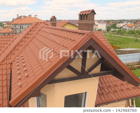 House with a new roof made of orange metal. View from above. Corrugated metal roof and metal roofing. Modern roof made of met House with a new roof made of orange metal. View from above. Corrugated metal roof and metal roofing. Modern roof made of met 142988760