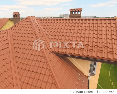 House with a new roof made of orange metal. View from above. Corrugated metal roof and metal roofing. Modern roof made of met 142988762