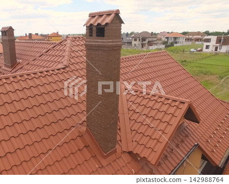 House with a new roof made of orange metal. View from above. Corrugated metal roof and metal roofing. Modern roof made of met House with a new roof made of orange metal. View from above. Corrugated metal roof and metal roofing. Modern roof made of met 142988764