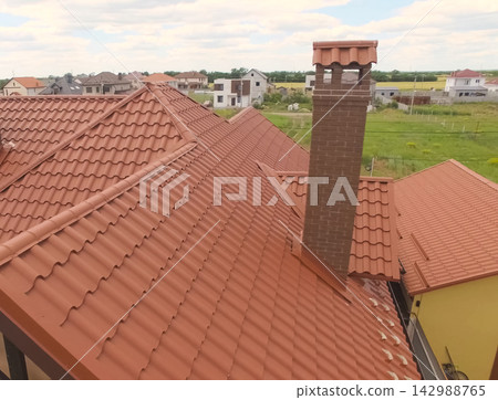 House with a new roof made of orange metal. View from above. Corrugated metal roof and metal roofing. Modern roof made of met House with a new roof made of orange metal. View from above. Corrugated metal roof and metal roofing. Modern roof made of met 142988765