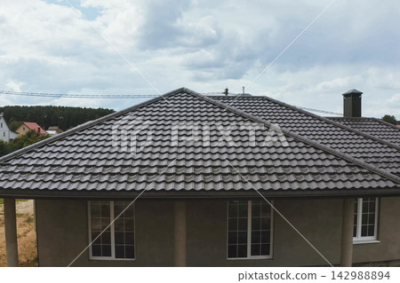 House with a brown metal roof.Corrugated metal roof and metal roofing. Modern roof made of metal. 142988894