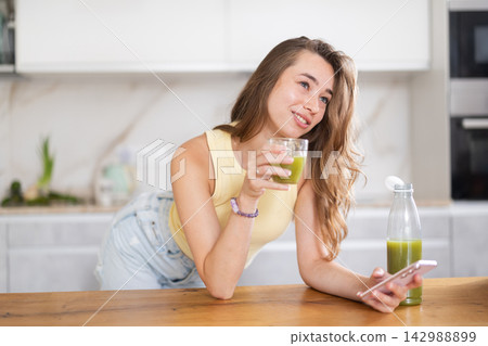 Young woman drinking juice and scrolling through social media on mobile Young woman drinking juice and scrolling through social media on mobile 142988899