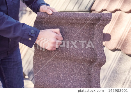 Sheet of polymer roof tiles. worker holds a sheet of polymer plastic tile and bangs on it with his fist. Sheet of polymer roof tiles. worker holds a sheet of polymer plastic tile and bangs on it with his fist. 142988901
