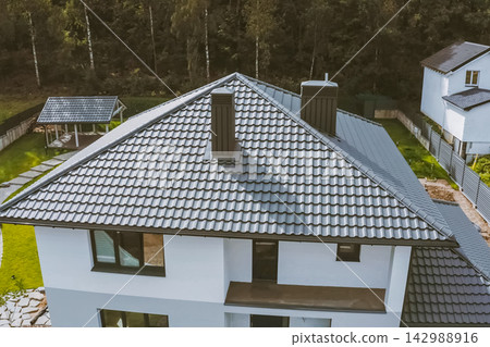 House with a gray metal roof. Corrugated metal roof and metal roofing. Modern roof made of metal. House with a gray metal roof. Corrugated metal roof and metal roofing. Modern roof made of metal. 142988916
