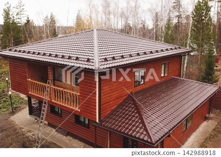 House with a brown metal roof.Corrugated metal roof and metal roofing. Modern roof made of metal. House with a brown metal roof.Corrugated metal roof and metal roofing. Modern roof made of metal. 142988918