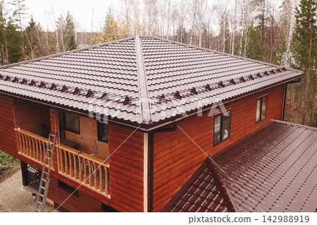 House with a brown metal roof.Corrugated metal roof and metal roofing. Modern roof made of metal. House with a brown metal roof.Corrugated metal roof and metal roofing. Modern roof made of metal. 142988919