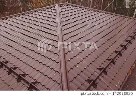 House with a brown metal roof.Corrugated metal roof and metal roofing. Modern roof made of metal. 142988920
