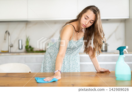 Girl in sundress cleans cupboards and furniture in kitchen Girl in sundress cleans cupboards and furniture in kitchen 142989026