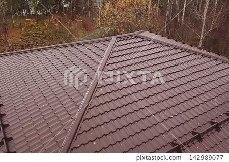 House with a brown metal roof.Corrugated metal roof and metal roofing. Modern roof made of metal. House with a brown metal roof.Corrugated metal roof and metal roofing. Modern roof made of metal. 142989077