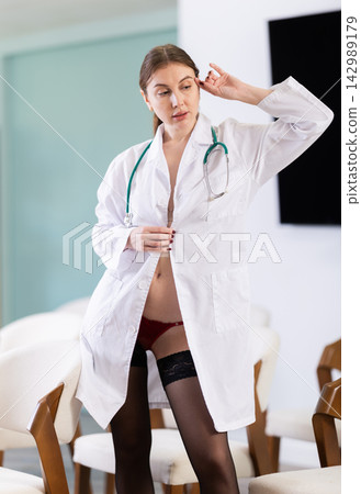 Young woman doctor in lab coat and lingerie posing in lecture hall Young woman doctor in lab coat and lingerie posing in lecture hall 142989179
