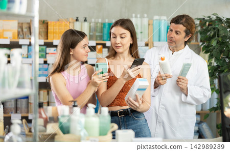 Woman with teen girl choosing and scan QR code cream at pharmacy. Man pharmacist offer European brand Woman with teen girl choosing and scan QR code cream at pharmacy. Man pharmacist offer European brand 142989289